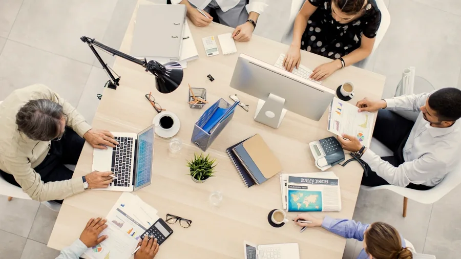 Equipa reunida à volta de uma mesa de escritório com portáteis, vista de cima